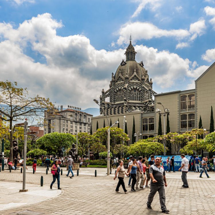 Medellin, Colombia - March 26, 2018: Tourists walking at Botero Plaza in Medellin, Colombia.   At the background is Palace of Culture Rafael Uribe and Coltejer Building, symbols of the city.